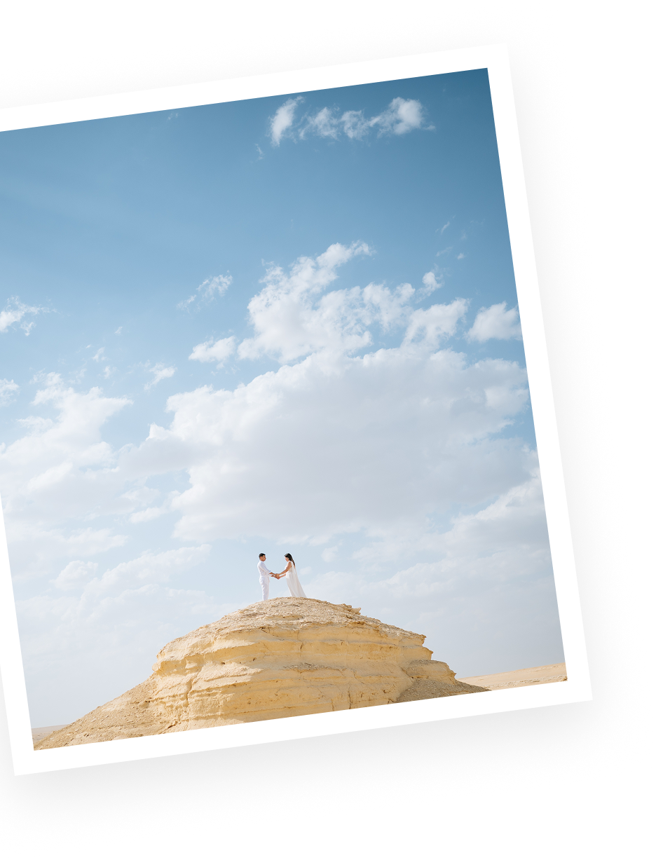 Couple standing on a yellow rock formation under a blue sky with scattered clouds